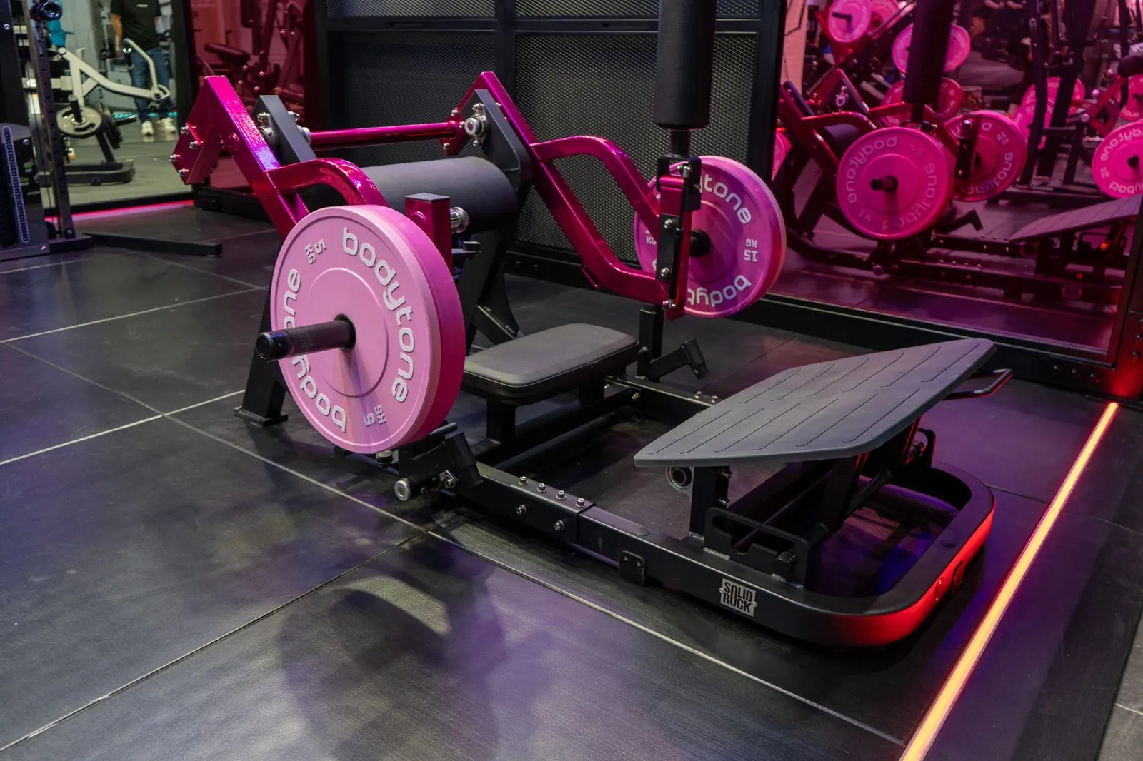 Hip-Thrust-Station der Bodytone Booty Area mit pinken Hantelscheiben und magentafarbenem Rahmen.
